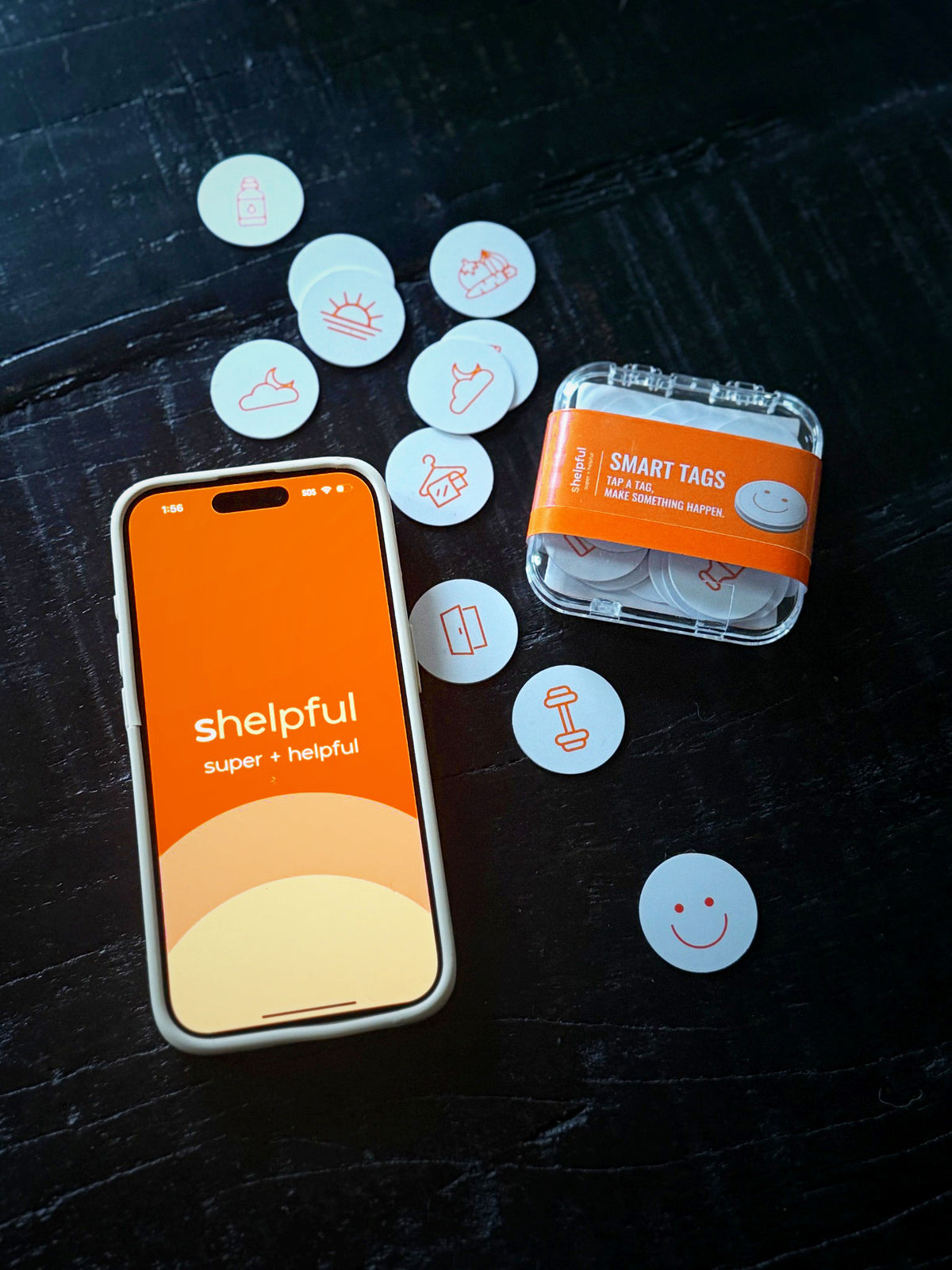 Shelpful Smart Tags 20-pack in a slick acrylic case, surrounded by white NFC sticker tags with orange icons, next to a phone showing the Shelpful app
