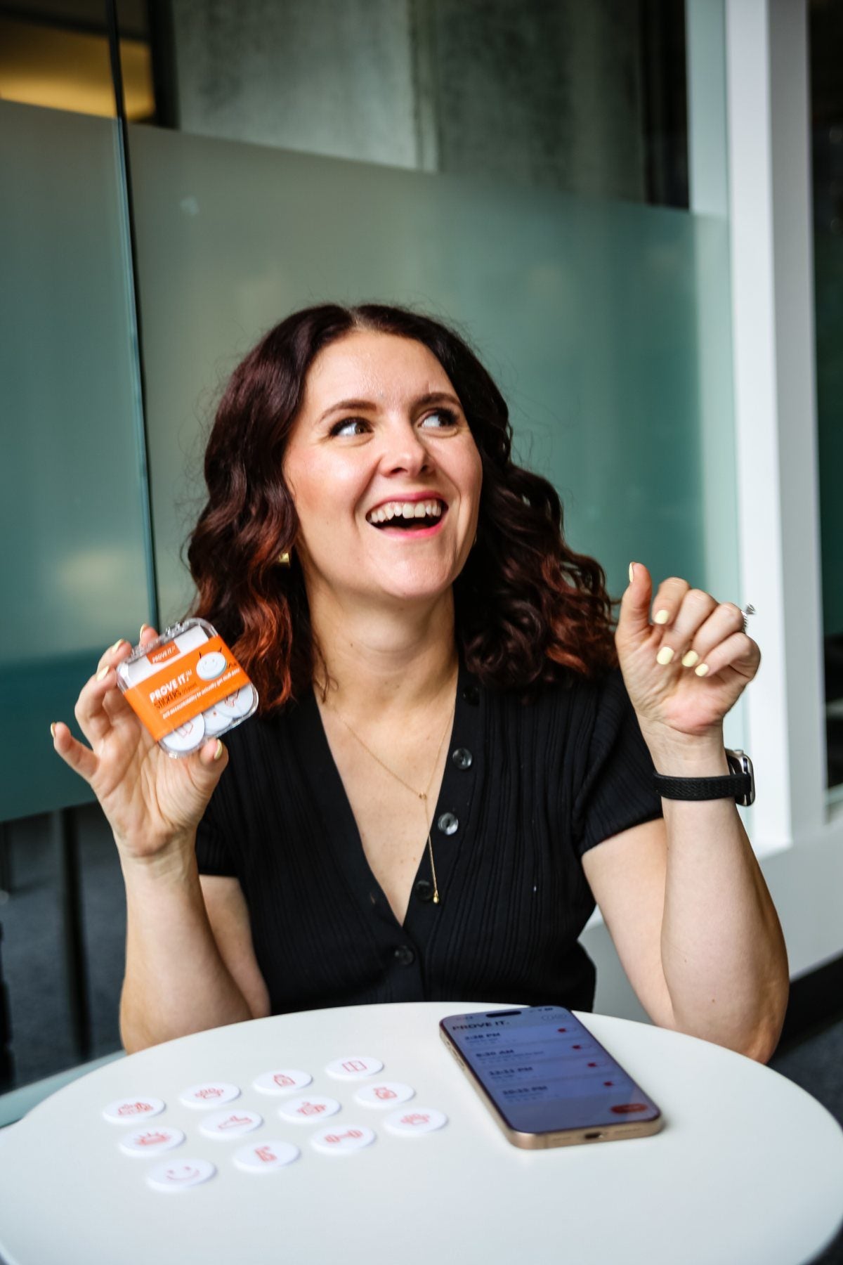 Sharon laughing and holding a PROVE IT case next to stickers and the app